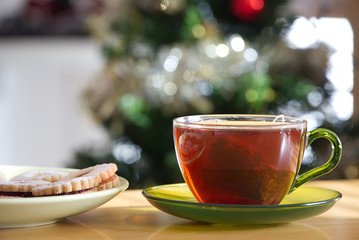 A cup of black tea a plate of cookies with a blurred Christmas tree at the background                            