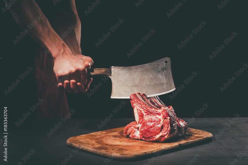 Wall mural butcher cutting raw meat with cleaver on wooden cutting board