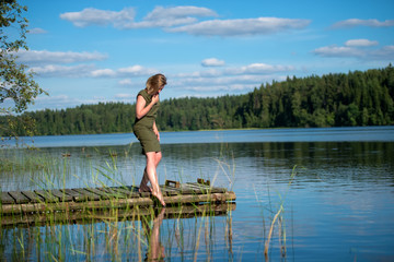 Beautiful girl touches the water standing on a wooden jetty at a lake