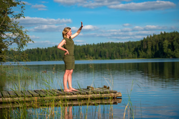 Fototapeta na wymiar Beautiful girl waving standing on a wooden jetty at a lake