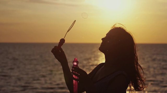 Happy brunette woman blowing soap bubbles on the beach at beautiful sunset by the sea. Slow motion. 1920x1080