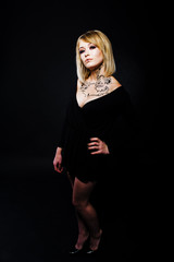 Studio portrait of blonde girl with originally make up on neck, wear on black dress at dark background.