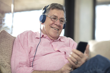 Smiling senior man wearing headphones listening to music at home