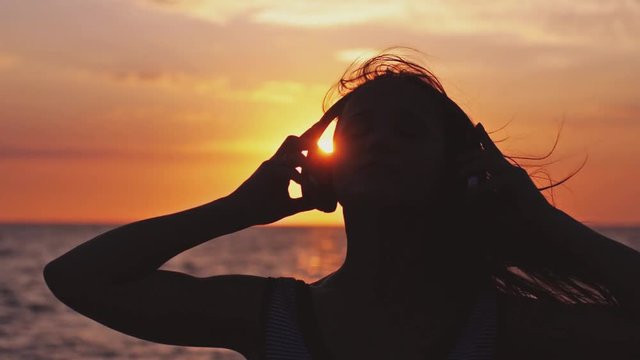 Silhouette of girl wearing headphones have fun listening music on the beach at amazing sunset in slow motion. 1920x1080