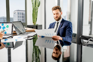 Handsome analytic manager working with paper charts and laptop at the luxury office interior