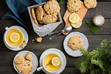 The perfect tasty breakfast!)  Oatmeal cookies with chocolate in wooden box and green tea with lemon in mugs on a dark background with a Xmas tree. Best useful Cookies.  Flat lay, top view