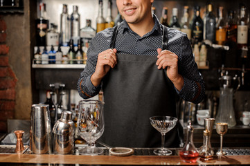 Smiling bartender standing behind the bar counter with a bar equipment