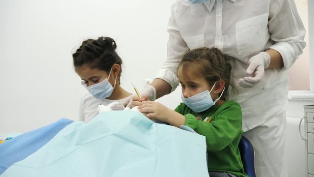 Children treat a toy with dentist using a diferent dental tools. Two little girl play the roles of dentist during a dental check-up. Moves a dental chair.