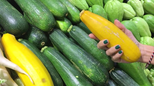 Woman choosing fresh organic green and yellow zucchini at the market. Asia, Indonesia.