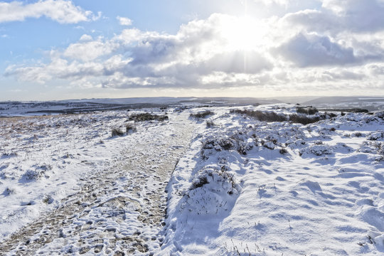 The winter sun pokes through the clouds lighting up the snow covered Peak District landscape