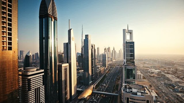 Dubai skyscrapers at sunset. Scenic aerial view over famous highway with fast moving traffic and financial center towers. Timelapse.