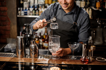 Smiling bartender putting a big ice cube using special ice tongs