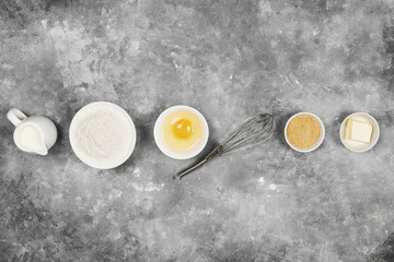 Obraz na płótnie Canvas Ingredients for pastries - flour, eggs, butter, milk, sugar on a gray background. Top view. Food background
