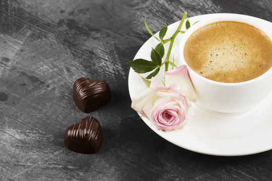 Espresso coffee in a white cup, a pink rose and chocolates on a dark background