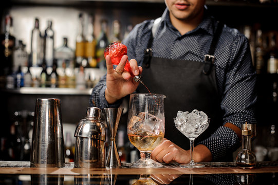 Barman pouring sweet fruit syrup into the large cocktail glass
