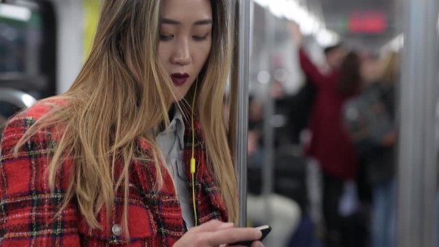young woman underground using smart phone listening music - technology, commuting, traveller concept
