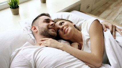 Closeup of young beautiful and loving couple talk and hug into bed while waking up in the morning.