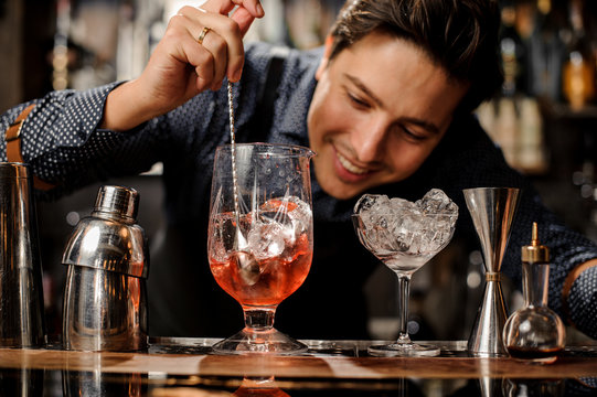 Young smiling barman stirring fresh alcoholic cocktail with syrups