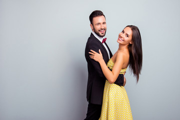 Portrait with copy space of love story of cute, cheerful, attractive, sexy couple in elegant outfit, tux, hugging, dancing, looking at camera, standing over grey background on party