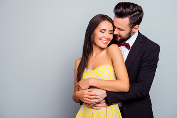Photo  of beautiful, cheerful, positive, cute, sensual, tender couple  enjoying hugs with each other having eyes close over grey background  with copy space, gentle husband's hands touch his wife