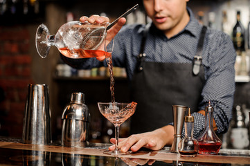 Bartender adding red alcoholic drink into cocktail glass