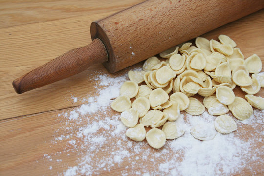 Fresh orecchiette. Italian traditional pasta on wooden table with flour and wooden rollin pin