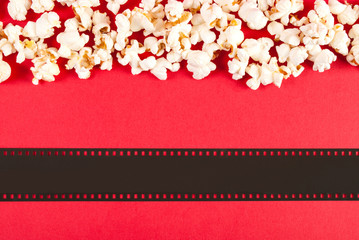Popcorn and film tape on red background, top view and space for text