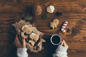 Woman holding box with Christmas cookies and drinking coffee on wooden table. Top view 