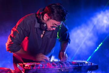 Portrait of active pretty young DJ woman playing music on laser lighting background