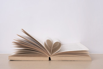 Page of book curved into heart shape on wood table. valentine concept.