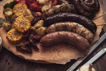 Grilled different meat and fish sausages with vegetables and spices on wooden background