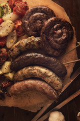 Grilled different meat and fish sausages with vegetables and spices on wooden background