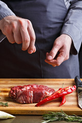 Chef seasoning rib eye steak on wooden board at restaurant kitch