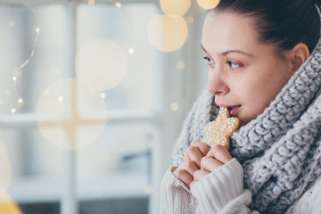 Close up of woman eating cookie next to the window. Winter theme
