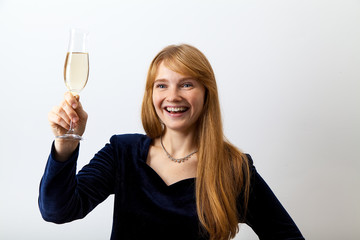 Portrait of young elegant lady with red hair and freckles dressed in dark velvet holding a glass of champagne and looking aside with a happy smile as if talking to somebody.