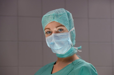 A young woman poses  in an operation theater  fully dressed as a theater nurse with a face mask  and green sterile medical work clothing.