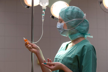 A young woman poses  in an operation theater  fully dressed as a theater nurse with a face mask  and green sterile medical work clothing.
