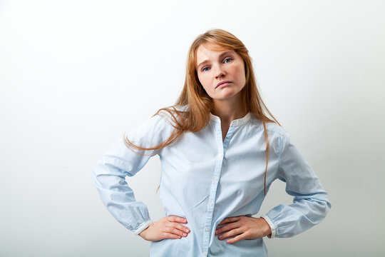 Horizontal image of young beautiful  lady with red hair and freckles dressed in casual blue shirt looking at the camera with confidence and indifference. White background, copy space.
