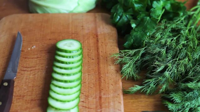 The cook slicing with a knife a fresh green cucumber on a wooden board
