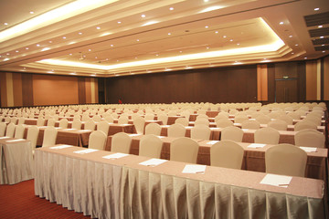 Prepare a conference room with the placement of the chairs style theater with chairs on the ground, the red carpet wearing a Skirt. The front side has shelves with raised area with located microphone.