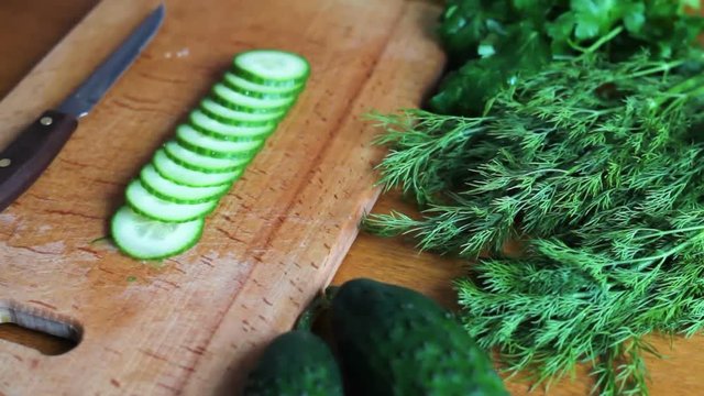 The cook slicing with a knife a fresh green cucumber on a wooden board