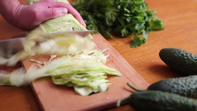 The cook slicing with a knife a fresh green cabbage on a wooden board