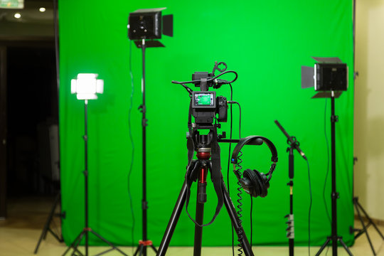 The camera on the tripod, led floodlight, headphones and a directional microphone on a green background. The chroma key. Green screen