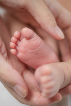 Mother's hand holding infant baby boy's feet with care.