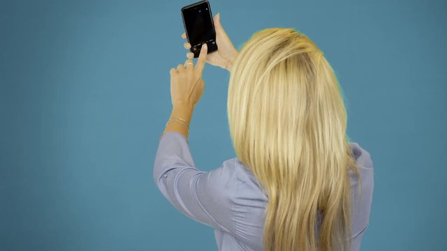 beautiful woman taking selfie using phone on blue background. Smiling and spinning enjoying lifestyle concept.