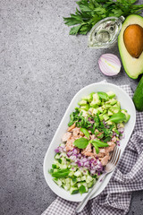 Healthy raw avocado tuna cucumber salad on concrete background. Top view, space for text.