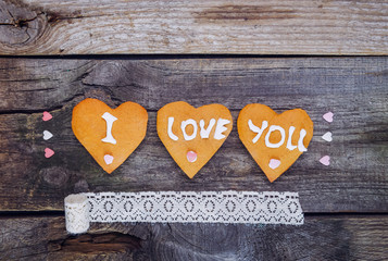 Homemade cookies in the form of heart with letteing I Love You and sweets sugar candy hearts, vintage ribbon on the rustic wooden background. Valentine day concept.. Selective focus. Space for text.