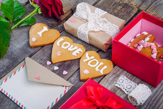 Festive composition with homemade cookies in shape of heart with I Love you lettering, rose, gift box. card, envelope, vintage ribbon. Gift for lover on Valentine's day. Selective focus, copy space.
