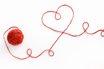 Wool ball and thread in shape of heart on white background