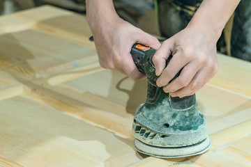 Сarpenter polishes the wooden surface of the door leaf. Electric eccentric orbital grinding...